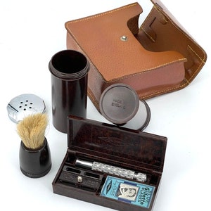 Puede incluir: Un estuche de viaje de cuero marrón vintage con un juego de afeitado. El juego incluye una brocha de afeitar, un recipiente de crema de afeitar, una navaja de afeitar y un paquete de cuchillas Gillette azules. El estuche está hecho en Inglaterra.