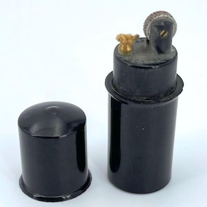 May include: A black vintage lighter with a wick and a black cap. The lighter has a silver top with a small wheel.