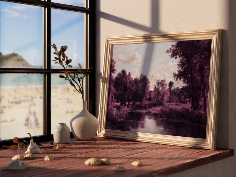 May include: A framed painting of a landscape with a river and trees in shades of purple and blue, hanging on a wall next to a window with a view of a beach.
