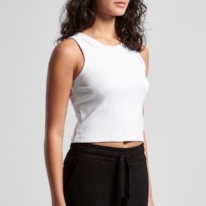 May include: A white ribbed tank top with a crew neck and a cropped fit. The model is also wearing black sweatpants. The top is a solid color and appears to be made of a soft, stretchy material.