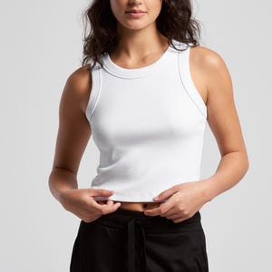 May include: A white ribbed tank top with a crew neck. The top is sleeveless and cropped, and the model is wearing black sweatpants. The top is made of a soft, ribbed material.