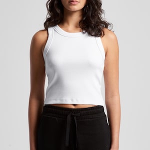 May include: A white ribbed tank top with a crew neck. The top is paired with black sweatpants with a drawstring. The model is standing in front of a white background.
