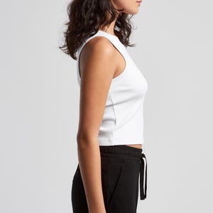 May include: A white ribbed tank top and black drawstring pants are shown in a side view. The tank top is sleeveless and cropped. The pants are loose-fitting with a drawstring waist. The background is plain.