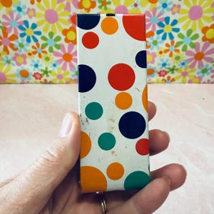 May include: A white metal box with a colorful polka dot pattern. The dots are red, orange, yellow, green, and blue.