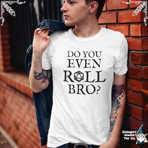 May include: White t-shirt with the text "DO YOU EVEN ROLL BRO?" in black. The shirt features a D20 die graphic. The shirt is being worn by a person. The shirt is from Gnaughty Gnome Tee Co.