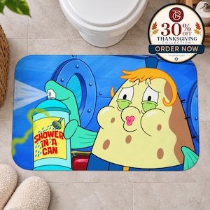 May include: A rectangular bath mat featuring a cartoon character with yellow skin and orange hair holding a blue spray can labelled Shower in a Can. The background shows a blue circular window and a blue wall. The character has a surprised expression.
