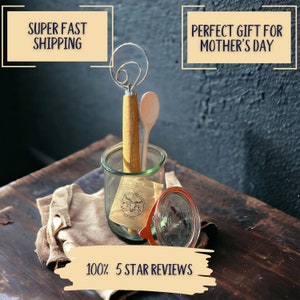 May include: A glass jar with a red lid filled with a wooden spoon and a dough whisk. The jar has a label with the text "Second Ave. Salt Co. Est. 2003". The jar is sitting on a brown cloth napkin.