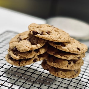 May include: A stack of freshly baked chocolate chip cookies on a black wire cooling rack.