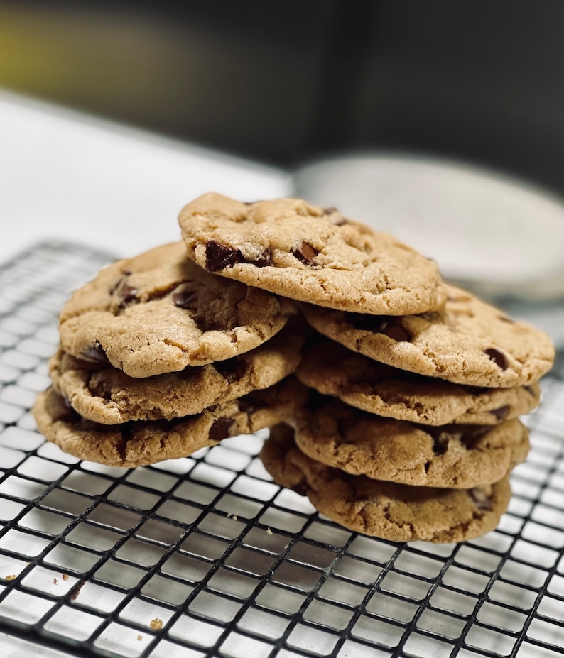 May include: A stack of freshly baked chocolate chip cookies on a black wire cooling rack.