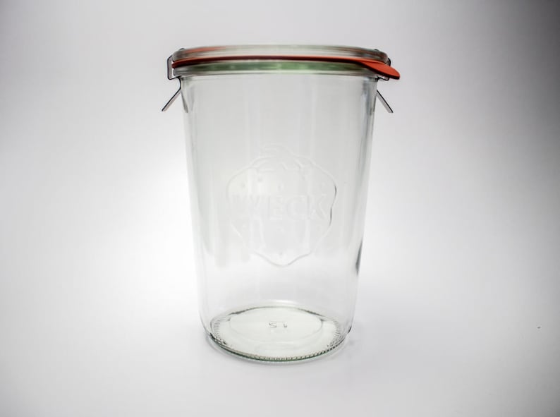May include: A clear glass jar with a wide mouth and a metal lid with a red rubber seal. The jar has a logo embossed on the side.
