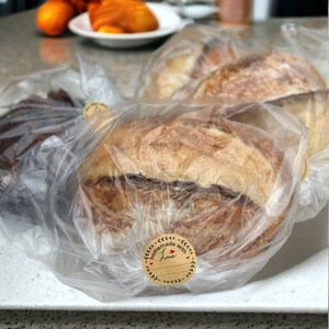 K&ouml;nnte beinhalten: Drei Brote in Plastikt&uuml;ten. Ein Brot hat einen braunen Papieretikett mit der Aufschrift "hausgemacht mit Liebe".