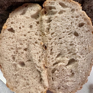 K&ouml;nnte beinhalten: Nahaufnahme eines geschnittenen Brotlaibs, der eine hellbraune, luftige Krume mit gro&szlig;en L&ouml;chern zeigt. Das Brot hat eine leicht unregelm&auml;&szlig;ige Form und eine weiche, fluffige Textur.