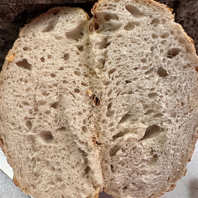 K&ouml;nnte beinhalten: Nahaufnahme eines geschnittenen Brotlaibs, der eine hellbraune, luftige Krume mit gro&szlig;en L&ouml;chern zeigt. Das Brot hat eine leicht unregelm&auml;&szlig;ige Form und eine weiche, fluffige Textur.