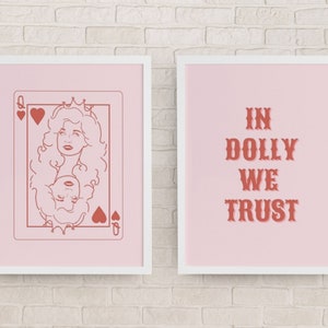 May include: Two framed prints with a pink background. The left print features a line drawing of Dolly Parton as the Queen of Hearts playing card. The right print features the text "In Dolly We Trust" in a red, stylized font.