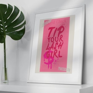 May include: A framed pink poster with white tape on the edges. The poster says "Guest Check" and "Tip Your Lash Girl" in pink lettering with a pink dollar sign and pink paint splatters.