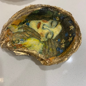 May include: A gold-rimmed, ceramic dish with a painted image of a woman's face with her eyes closed. The image is surrounded by a floral pattern.