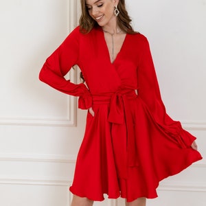 May include: A red satin wrap dress with long sleeves and a tie at the waist. The dress has a V-neckline and a ruffled hem.