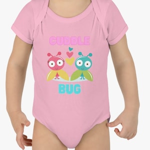 Puede incluir: Un body de bebé rosa con un gráfico de dos bichos de dibujos animados con corazones encima y el texto "Cuddle Bug".