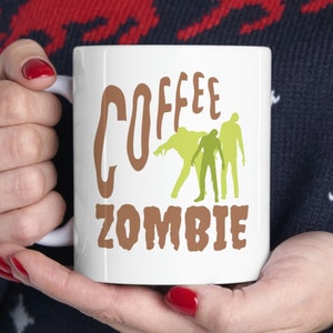 May include: White coffee mug with brown text that reads "Coffee Zombie" and a graphic of three green zombies.
