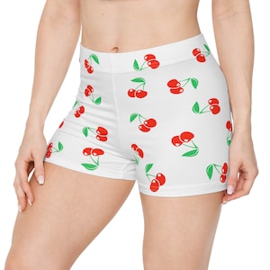 May include: White athletic shorts with a red cherry print. The cherries are scattered across the fabric in a repeating pattern.