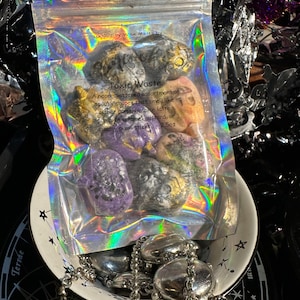 Puede incluir: Una bolsa de fundidos de cera de soja en una variedad de formas y colores espeluznantes. La bolsa está etiquetada como "Toxic Waste" y dice "Un surtido de formas espeluznantes salpicadas de neón que huelen a latte de especias de calabaza, crema de caramelo de calabaza o palitos de duendes azucarados 2.5oz".