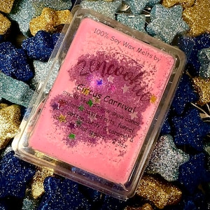 May include: A pink soy wax melt in a clear plastic container with glitter. The wax melt is labelled "100% Soy Wax Melts by ZenMood" and "Circus Carnival". The label also describes the scent as "smells like rainbow snow cones, popcorn, roasted nuts, funnel cake cotton candy & caramel & candy coated apples, 2.5oz".