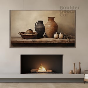 Pode incluir: Uma pintura emoldurada de uma natureza-morta com cerâmica. A pintura apresenta um pote de barro marrom, um pote de barro preto, uma pequena tigela de barro marrom e três pequenos potes de barro branco. A cerâmica está disposta em uma mesa de madeira com um fundo marrom claro. A pintura é intitulada "Boulder Goods Co."