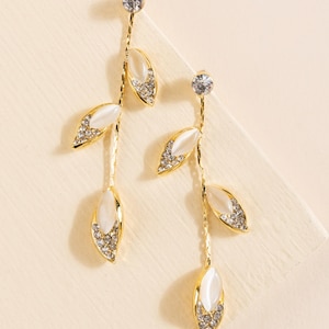 May include: Gold dangle earrings with white pearlescent leaves and clear crystal accents.
