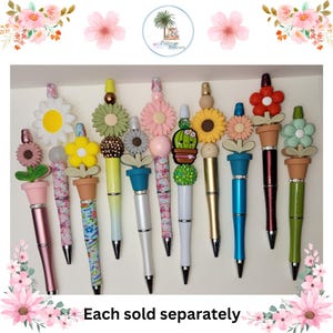 May include: A collection of 10 colorful pens with flower and plant designs. Each pen features a different flower or plant, including a sunflower, a cactus, and a daisy. The pens are all decorated with beads and glitter. Each sold separately.