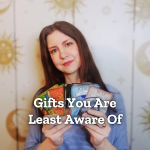 May include: A person holding a deck of oracle cards with the text "Gifts You Are Least Aware Of." The cards have various colorful designs and the words "Iceberg" and "Wolf" are visible on two of the cards.