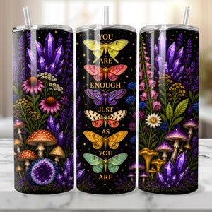 May include: A stainless steel tumbler with a black background featuring colorful butterflies, flowers, mushrooms, and crystals. The text "YOU ARE ENOUGH JUST AS YOU ARE" is displayed on the tumbler. Includes a straw.