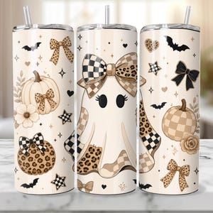 May include: Three cylindrical tumblers with lids and straws featuring a cream background decorated with ghosts, pumpkins, leopard print bows, checkered patterns, bats, stars, and hearts in shades of brown, black, and beige.