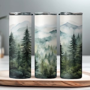Pode incluir: Três canecas isoladas de aço inoxidável com uma cena de floresta em aquarela. O design apresenta árvores altas de folhas perenes, montanhas nebulosas e uma paleta de cores suaves de verdes, azuis e brancos. Cada caneca tem uma tampa prateada.
