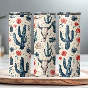 May include: Three stainless steel tumblers with a cream background and a repeating pattern of cacti, flowers, and cow skulls. The tumblers are all the same size and have a lid.