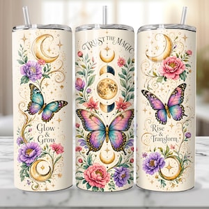 May include: Three cylindrical tumblers with straws, featuring a cream background with floral, butterfly, and moon phase illustrations. Text includes "Glow & Grow", "Trust the Magic", and "Rise & Transform" in elegant black script lettering.