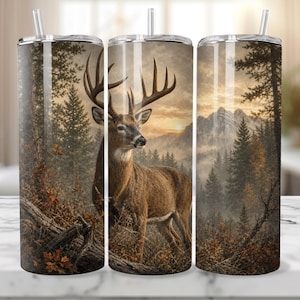 May include: A cylindrical stainless steel tumbler featuring a wrap-around print of a brown deer with large antlers standing in a forest landscape with pine trees, fallen logs, and mountains in the background under a golden sunset sky with a straw.