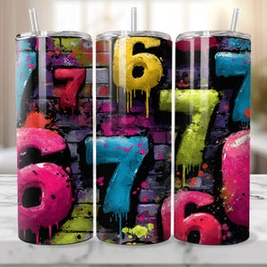 Puede incluir: Tres vasos aislados de acero inoxidable con tapas y pajitas. Cada vaso presenta un diseño de estilo grafiti con los números 6 y 7 en colores brillantes sobre un fondo de pared de ladrillo. Los colores incluyen rosa, amarillo, azul y verde.