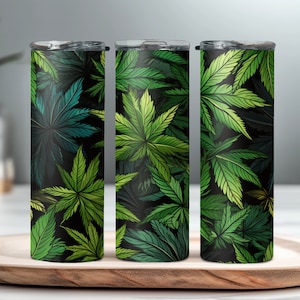 May include: Three stainless steel tumblers with a black background and a green leafy pattern. The tumblers are lined up in a row on a wooden surface.