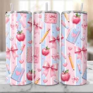 Könnte beinhalten: Drei Edelstahlbecher mit einem rosa, blauen und weißen Streifenmuster. Das Design umfasst rosa Schleifen, Äpfel, Bleistifte, Herzen und Notizbücher. Jeder Becher hat einen Strohhalm.