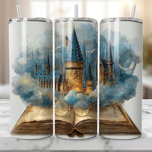 Könnte beinhalten: Edelstahl-Reisebecher mit einer Aquarellillustration eines Schlosses mit blauen Türmen und goldenen Akzenten, vor einem bewölkten Himmel. Das Design umfasst ein offenes Buch mit Brille, das ein Fantasy-Thema hervorruft.