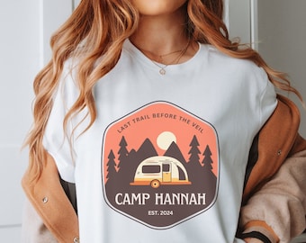 May include: White t-shirt with a vintage-style camping logo. The logo features a camper van, mountains, trees, and the text "Last Trail Before The Veil Camp Hannah Est. 2024".