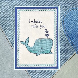 May include: A white card with a blue whale and the text "I whaley miss you" in blue embroidery. The card has a blue and white border.
