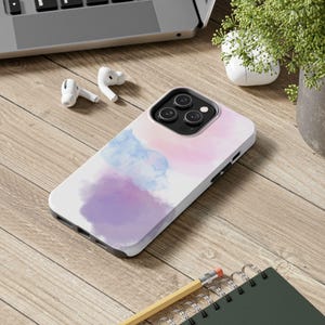 May include: A smartphone case featuring a soft watercolor design with blended patches of light blue, lavender, and pale pink. The case has a black camera cutout area with three circular lenses and a flash, designed to fit a modern mobile device.