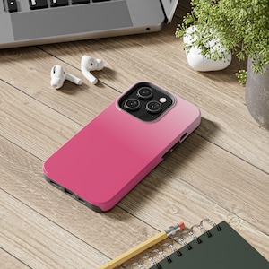 May include: A smartphone case featuring a vibrant pink gradient design that transitions from a deep magenta at the bottom to a lighter shade of pink at the top. The case includes a black camera cutout area with three circular lenses and a flash.