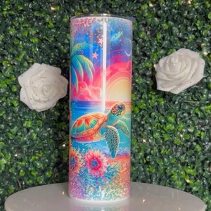 Könnte beinhalten: Zylindrischer Becher mit einem farbenfrohen Design einer Meeresschildkröte, Palmen und einem Sonnenuntergang über dem Ozean. Das Kunstwerk ist hell und farbenfroh, mit einem Blumenmuster am Boden. Der Becher ist wahrscheinlich aus Edelstahl.