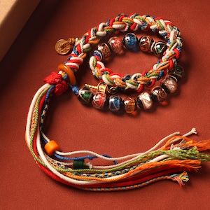 May include: A multi-colored braided cord necklace with a tassel and a variety of colorful glass beads.