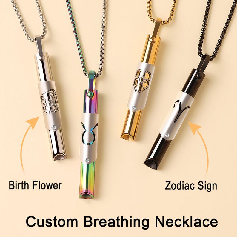 May include: Three silver, gold, and black necklaces with pendants that are hollow tubes with a small crystal at the bottom. The pendants have different designs, including a flower, a zodiac sign, and a bull. The necklaces are labelled "Birth Flower", "Zodiac Sign", and "Custom Breathing Necklace".