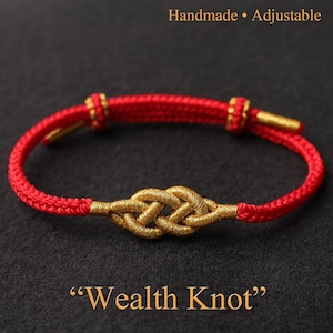 Può includere: Braccialetto regolabile fatto a mano, rosso e oro, con un design a nodo di ricchezza dorato. Il braccialetto è realizzato in cordoncino rosso con dettagli dorati. Il testo "Wealth Knot" è visualizzato sotto.