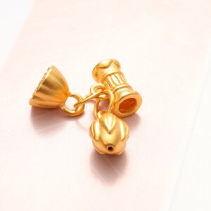 May include: Gold-toned metal charm with a flower-shaped design and a cylindrical bead with a decorative pattern.