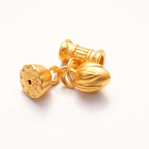 May include: Gold-toned metal jewelry findings with a lotus flower design. The findings are connected by a chain and have a decorative, textured finish.
